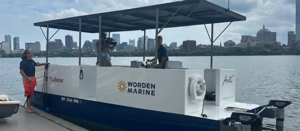 Worden Marine solar-powered boat on the Charles River, with a city skyline in the background.